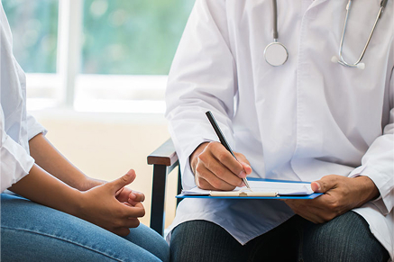 A doctor sitting with a patient in a bright, modern clinic office, writing on a chart